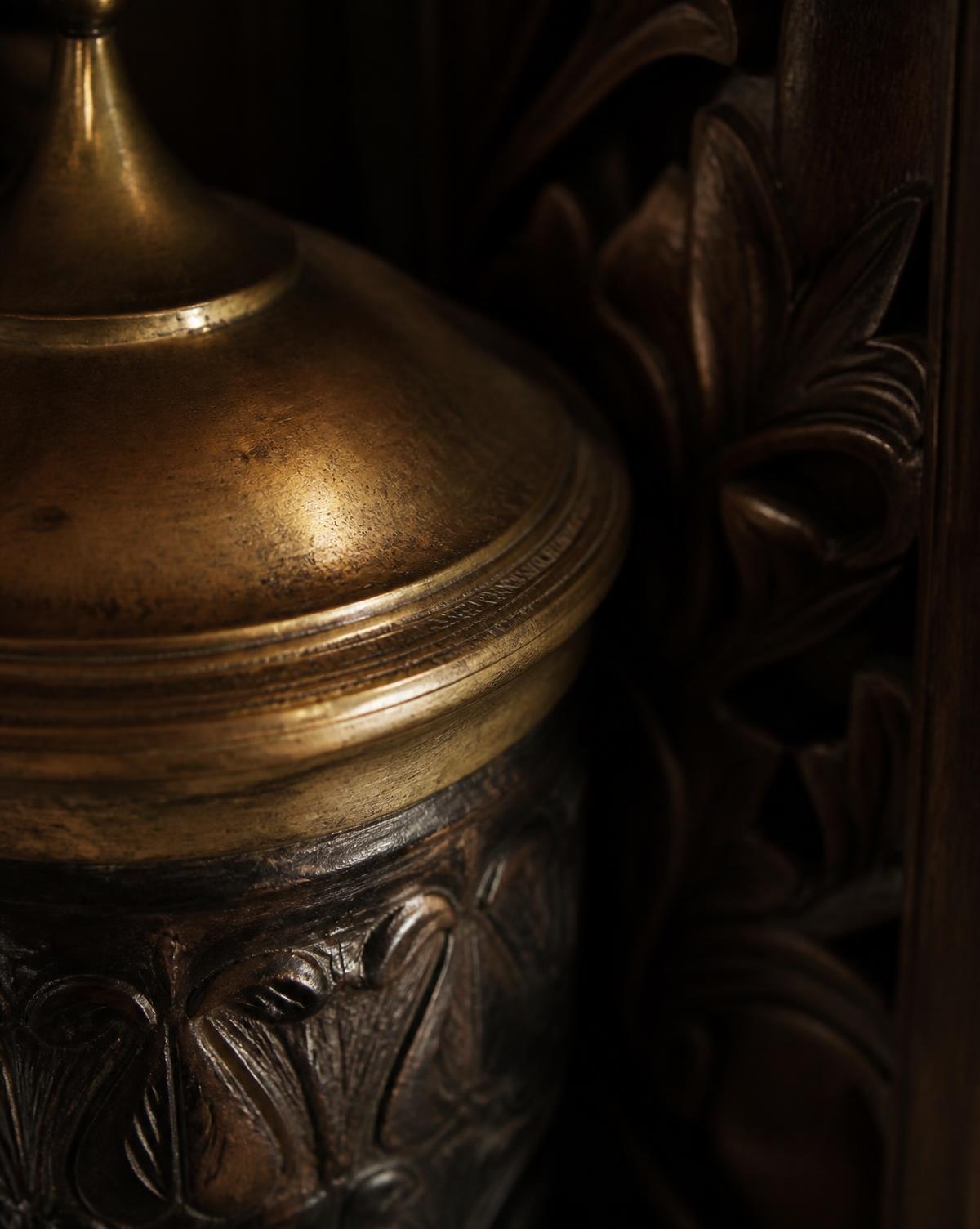 Close detail of an aged brass urn against carved dark wood